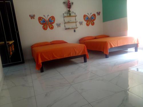 two beds in a room with orange sheets and butterflies on the wall at Casa Santuario Hotel Boutique in Guadalajara
