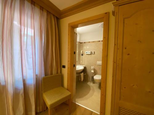 a bathroom with a toilet and a chair and a mirror at Boutique Hotel Diana in Madonna di Campiglio