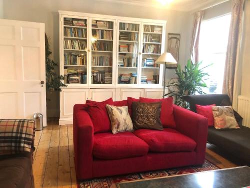 a red couch in a living room with a book shelf at Lauras Townhouse Apartments Thomas Street Townhouse in Bath