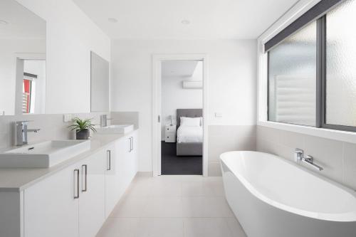 a white bathroom with two sinks and a bath tub at Phillip Island Townhouses in Cowes