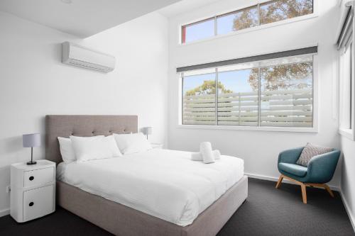 a white bedroom with a bed and a blue chair at Phillip Island Townhouses in Cowes
