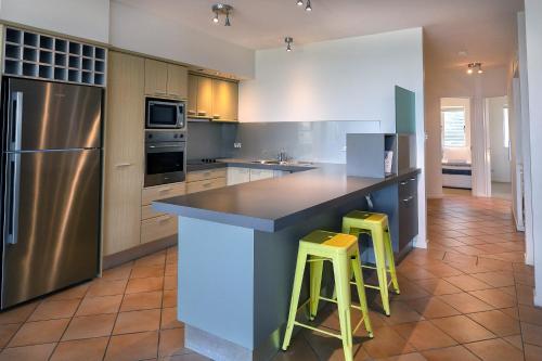 a kitchen with a large island with two yellow bar stools at Aqua Promenade Beachfront Holiday Apartments in Sunrise Beach