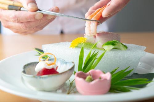 a person cutting a piece of sushi on a plate at Kikunan Onsen Yubel Hotel in Kumamoto