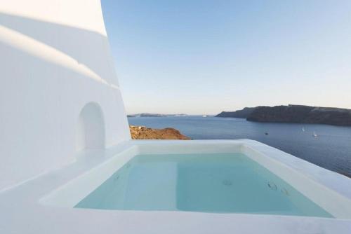 a white house with a swimming pool overlooking the ocean at The Architect's Cave House in Oia