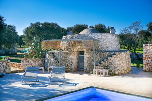 um edifício de pedra com duas cadeiras e uma piscina em Villa Artemide em Carovigno