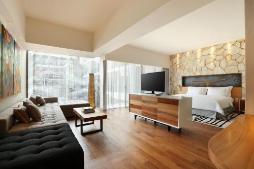 a hotel room with a bed and a tv and a couch at TS SUITES Seminyak Bali in Legian