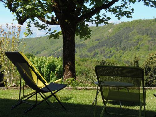 two chairs and a table in the shade of a tree at Hotel Les Mésanges in Saint-Martin-dʼUriage