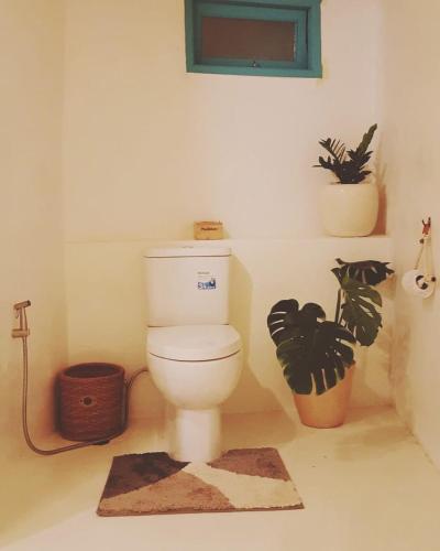 a bathroom with a toilet with two plants and a rug at Maliblues Bed & Art Gallery in Chumphon