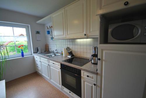 a kitchen with white cabinets and a sink and a microwave at Ferienwohnung Hörnmoor, 35586 in Uplengen