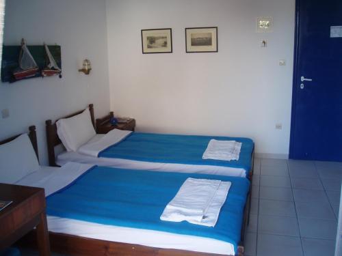 two twin beds in a room with blue sheets at Helios Hotel in Agia Marina Aegina