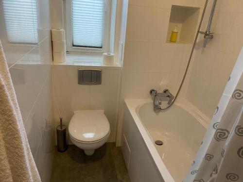 a white bathroom with a toilet and a bath tub at DK Apartament Reymonta in Olsztyn