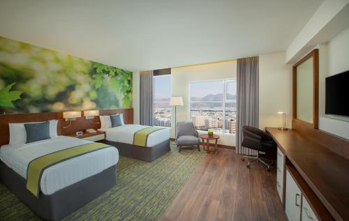 a hotel room with two beds and a desk at Wyndham Garden Muscat Al Khuwair in Muscat
