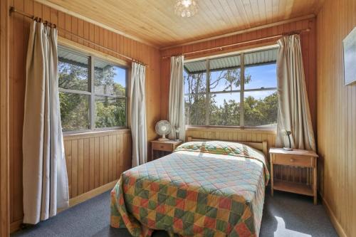 a bedroom with a bed and two windows at Alinjarra - 13 Waller Court in Point Lookout