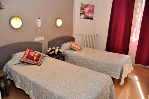 2 Betten in einem kleinen Zimmer mit roten Vorhängen in der Unterkunft Hotel Lux in Grenoble