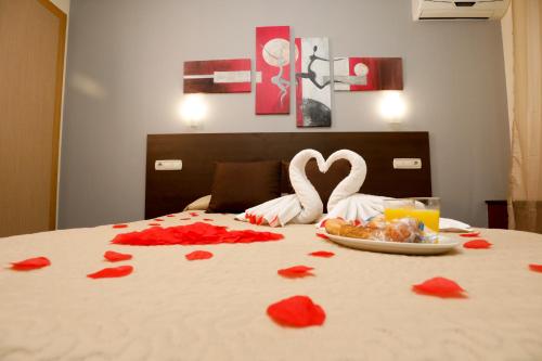 a bed with red rose petals on it with two swans and hearts at Hostal Conde David in Salamanca