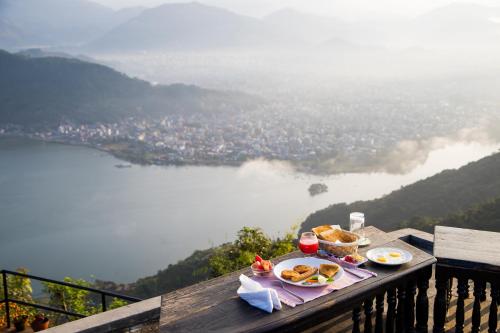 a table with food on it with a view of a lake at Raniban Retreat in Pokhara
