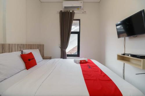 a bedroom with a white bed with red pillows and a television at RedDoorz Syariah near RSUD Siti Fatimah Palembang in Palembang