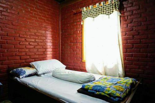 a bed in a room with a brick wall and a window at Oemah Kajoe Lembang in Lembang