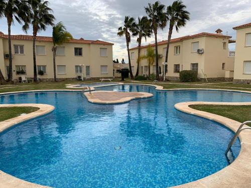 a large blue swimming pool with palm trees and buildings at OLIVA NOVA GOLF BEACH & RESORT club sevilla II in Oliva