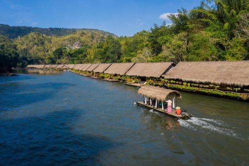 a river with a row of houses and a boat at River Kwai Jungle Rafts in Sai Yok