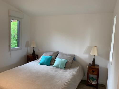 a bedroom with a white bed with two blue pillows at CHALET AU BORD DE LA SOMME in Hem-Monacu