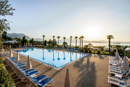 a large swimming pool with lounge chairs and palm trees at Onda Blu Resort in Manerba del Garda
