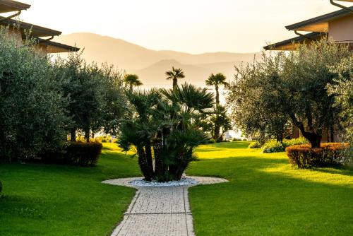 a garden with palm trees and a walkway at Onda Blu Resort in Manerba del Garda
