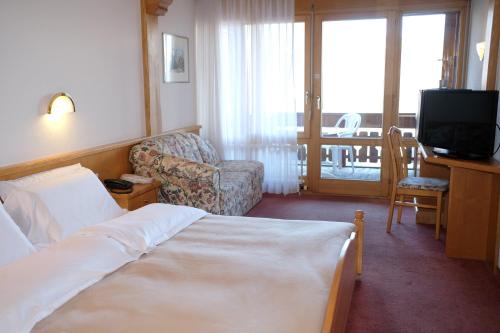 a hotel room with a bed and a chair and a television at Hotel Restaurant Rothorn in Visperterminen