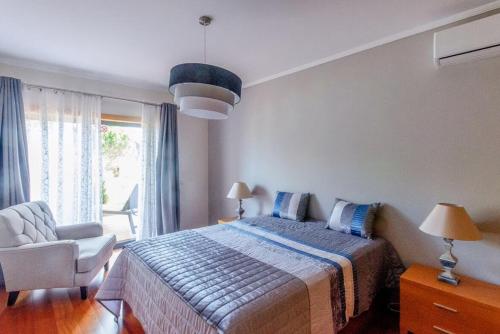 a bedroom with a bed and a chair and a window at Casa Sol Corcovada in Albufeira