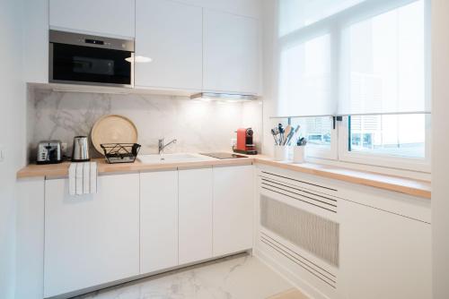 a white kitchen with white cabinets and a window at SUITE GIDE : au cœur de la Rive Gauche, neuf, design, 2/4 personnes in Paris