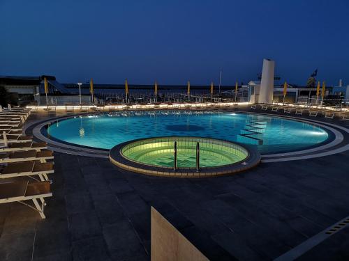 uma grande piscina à noite com luzes em Hotel David em Cesenatico
