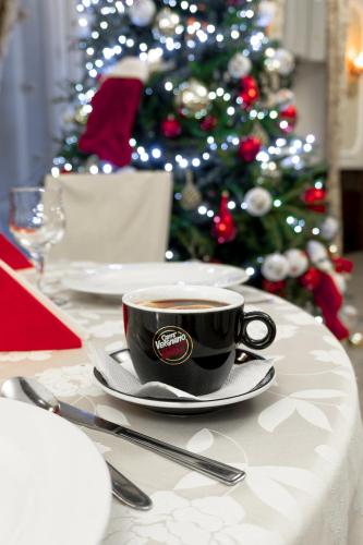 a cup of coffee on a table with a christmas tree at Pensiunea Splendid in Dorohoi