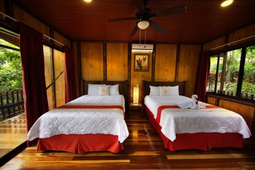 two beds in a room with wooden walls and windows at Heliconias Nature Inn in Fortuna