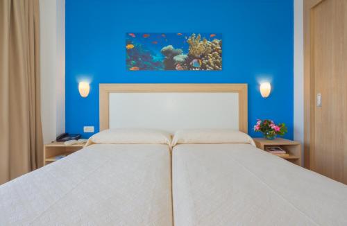 a bed with a blue and white bedspread and a painting on the wall at Apartamentos Centro Cancajos in Los Cancajos