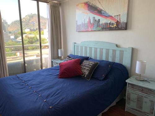 Un dormitorio con una cama azul con almohadas y una ventana en Depto. Excelente vista al Cerro San Cristobal !!, en Santiago