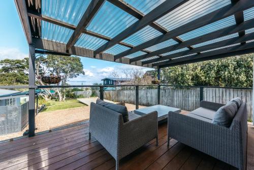a patio with two chairs and a table on a deck at Pohutukawa Cottage, Waiheke Island in Surfdale