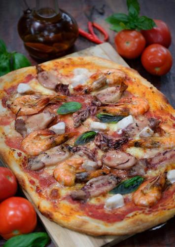 a pizza on a cutting board with shrimp and tomatoes at Amami Beachfront Villa with Private Beach in Puerto Galera