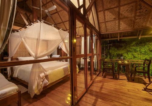 ein Schlafzimmer mit einem Himmelbett und einem Holzboden in der Unterkunft Kingfisher Ecolodge in Ban Kian-Ngông