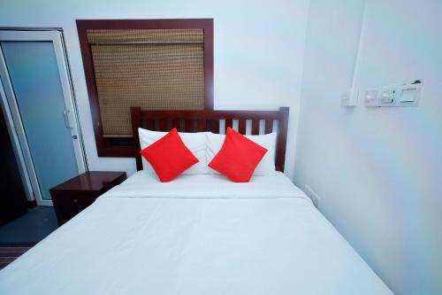 a white bed with two red pillows on it at Station Garden Hotel And Resturant in Jaffna