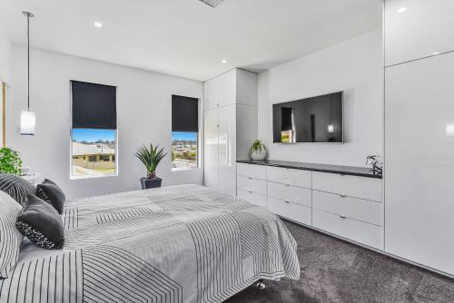 a white bedroom with a large bed and a flat screen tv at CONROE EXECUTIVE TOWNHOUSE - MODERN & STYLISH in Mount Gambier