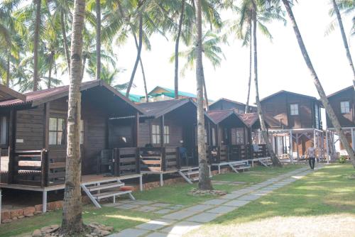 a row of wooden cottages with palm trees at Agonda Paradise in Agonda