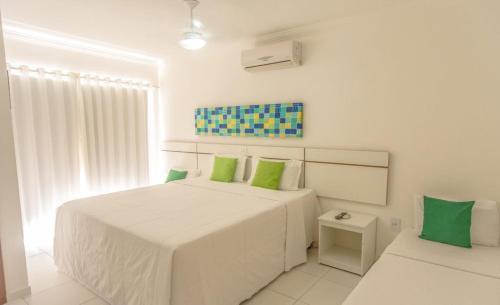 um quarto branco com uma cama grande e almofadas verdes em FLAT RESID MONT CARMELO em Porto Seguro