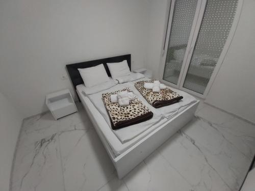a white bedroom with two beds and a window at XXL APARTMENTS CiTY CENTAR in Bitola
