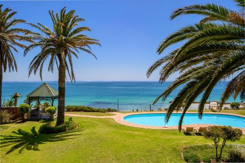 a swimming pool with palm trees and the ocean at Brookes Hill Suites Luxury Apartment 124 in Port Elizabeth