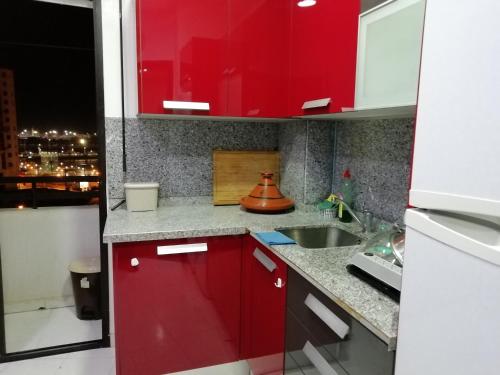 una cocina con armarios rojos y fregadero en appartement confortable, en Tánger