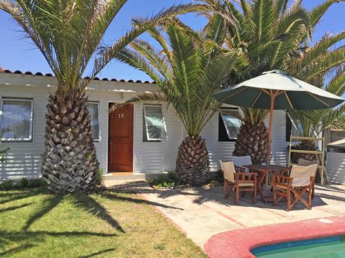 a house with palm trees and a table and an umbrella at Hotel y Cabañas La Rosa Nautica in Pichidangui