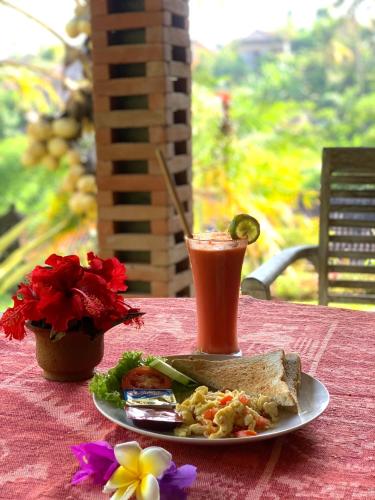 a plate with a sandwich and a drink on a table at Kukuh House Ubud in Ubud