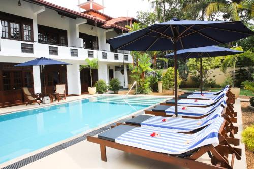 a group of lounge chairs with umbrellas next to a swimming pool at Sky and Sand Guesthouse in Beruwala