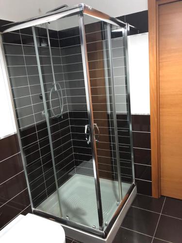a glass shower in a bathroom with black tiles at RAJA ROOMS in Alife
