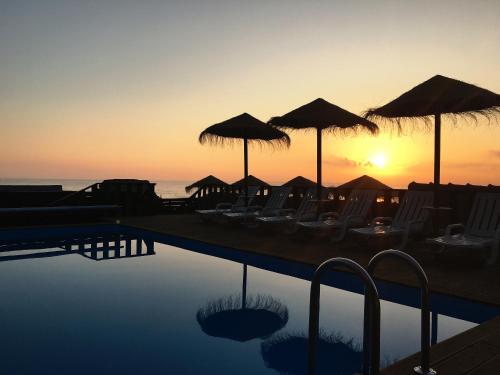 a pool with chairs and umbrellas with the sunset at Promar - Eco Beach & Spa Hotel in Maceira